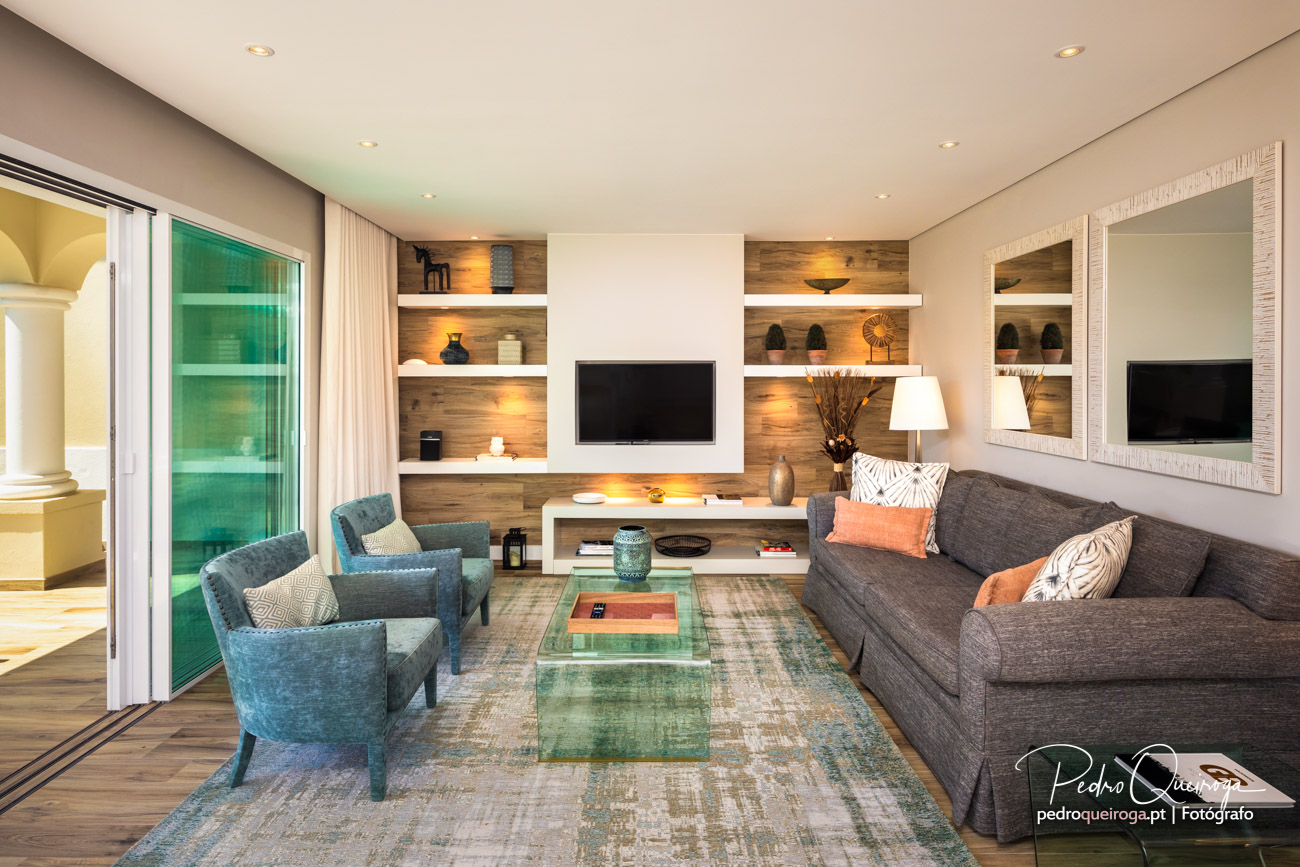 Sala de estar moderna com sofá cinza, poltronas azuis, parede com prateleiras em madeira e televisão embutida