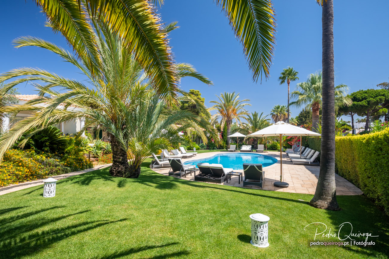 Jardim tropical luxuoso com piscina e espreguiçadeiras, perfeito para hotéis de charme no Algarve.