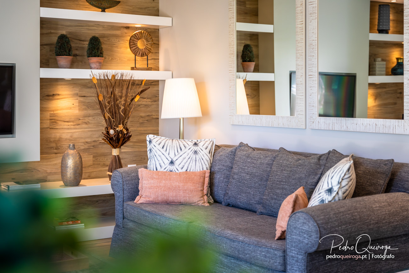 Sala de estar moderna com sofá cinzento, almofadas coloridas, estantes em madeira e iluminação ambiente acolhedora