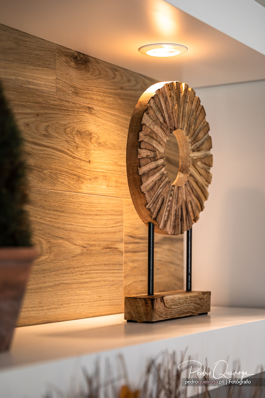 Escultura decorativa em madeira com formato circular apoiada em base de madeira maciça sobre superfície branca iluminada