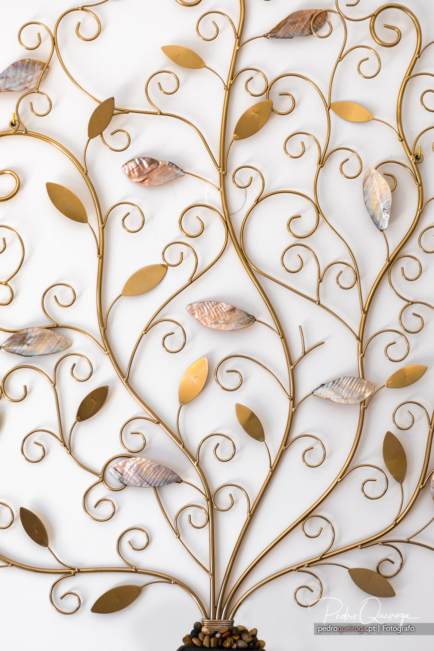 Peça decorativa em metal dourado com ramos ondulados, folhas douradas e nacaradas sobre fundo branco minimalista.