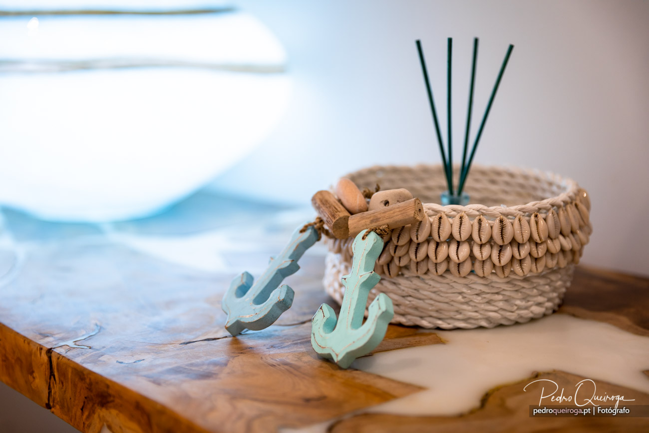 Cesto de vime com decoração costeira, âncoras verde-água e paus de incenso sobre mesa de madeira rústica