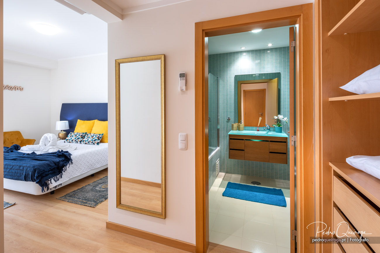 Suite ampla com casa de banho privativa em tons azul e madeira, ideal para valorizar o imóvel em fotografia de arquitetura