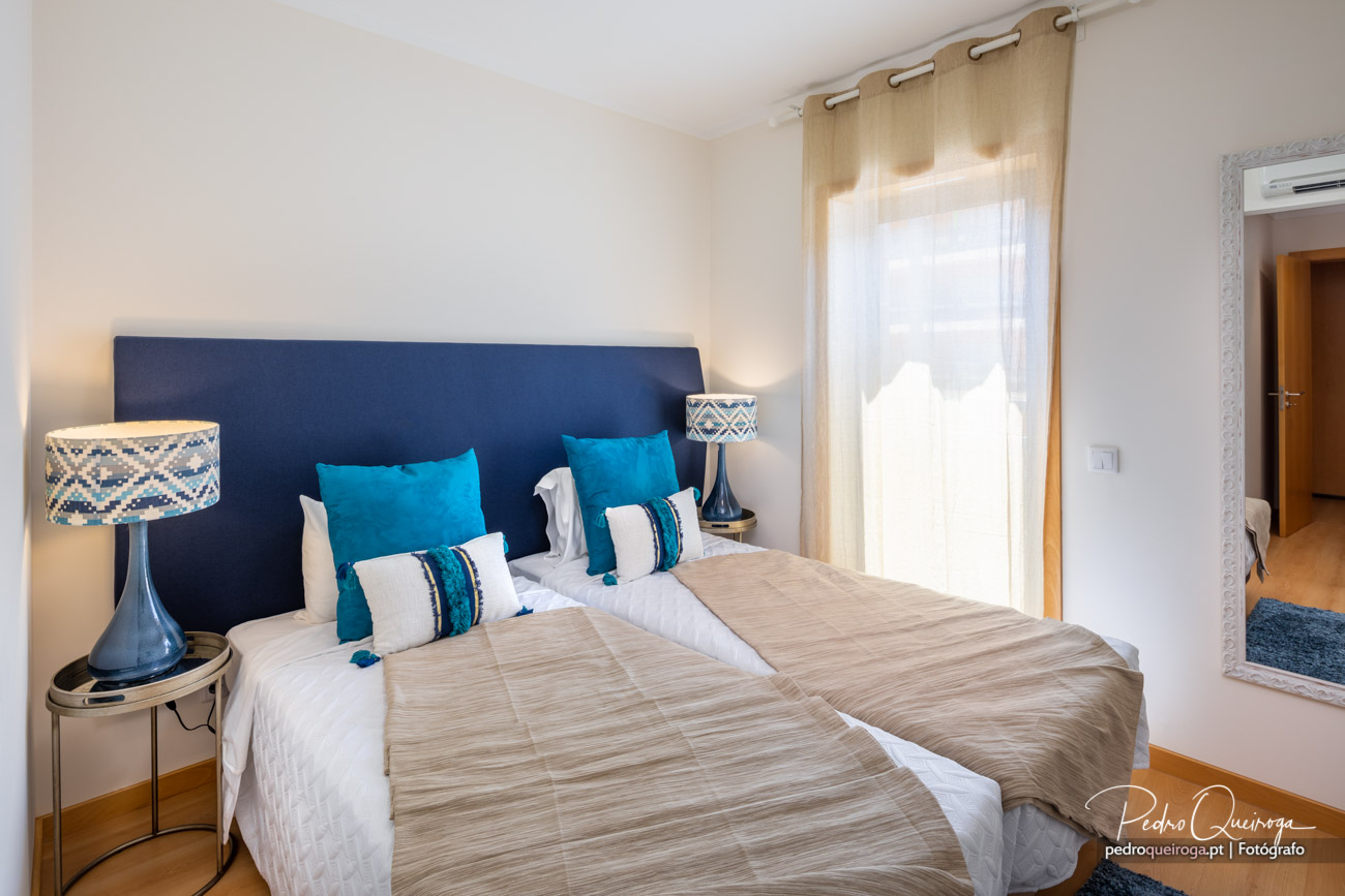 Quarto twin luminoso com cabeceira azul e almofadas turquesa, ideal para alojamento no Algarve