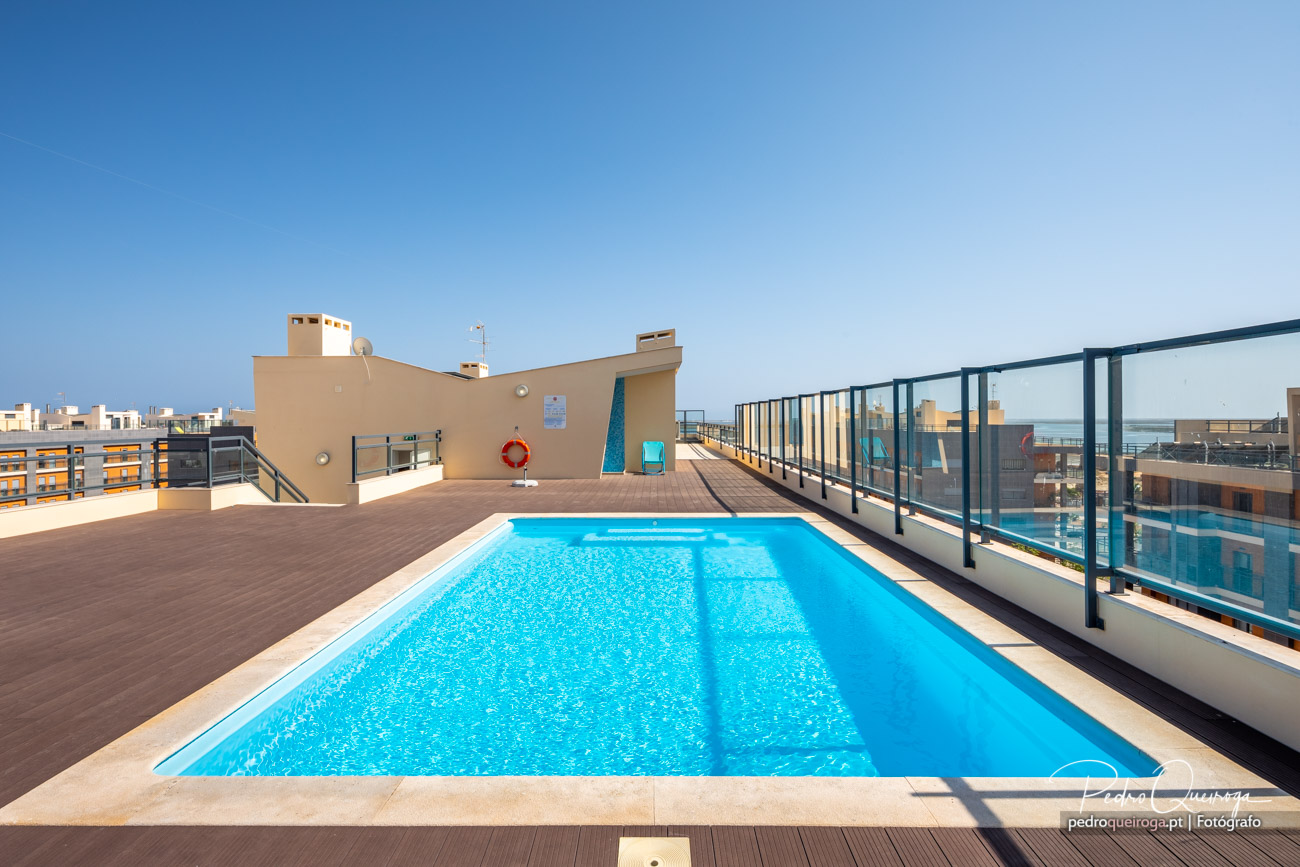 Piscina no terraço de condomínio moderno no Algarve, com vista para o mar e céu azul radiante