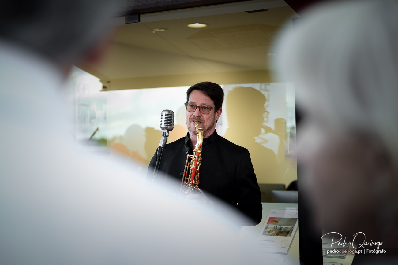 Músico de fato preto toca trompete ao lado de microfone vintage num ambiente interior elegante e luminoso