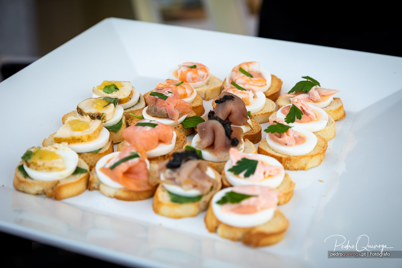 Travessa branca com canapés variados de camarão, salmão fumado e ovo cozido sobre tostas crocantes decoradas com salsa fresca