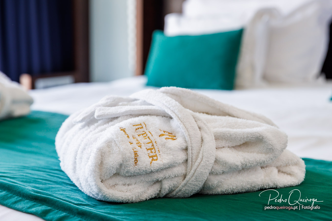 Roupão branco bordado sobre toalhões verdes numa cama, detalhe de conforto e elegância em hotéis de luxo