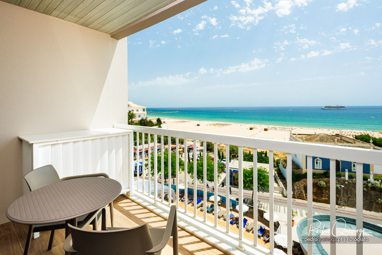 Varanda ampla com vista deslumbrante para praia de areia branca, mar turquesa e céu azul com nuvens dispersas