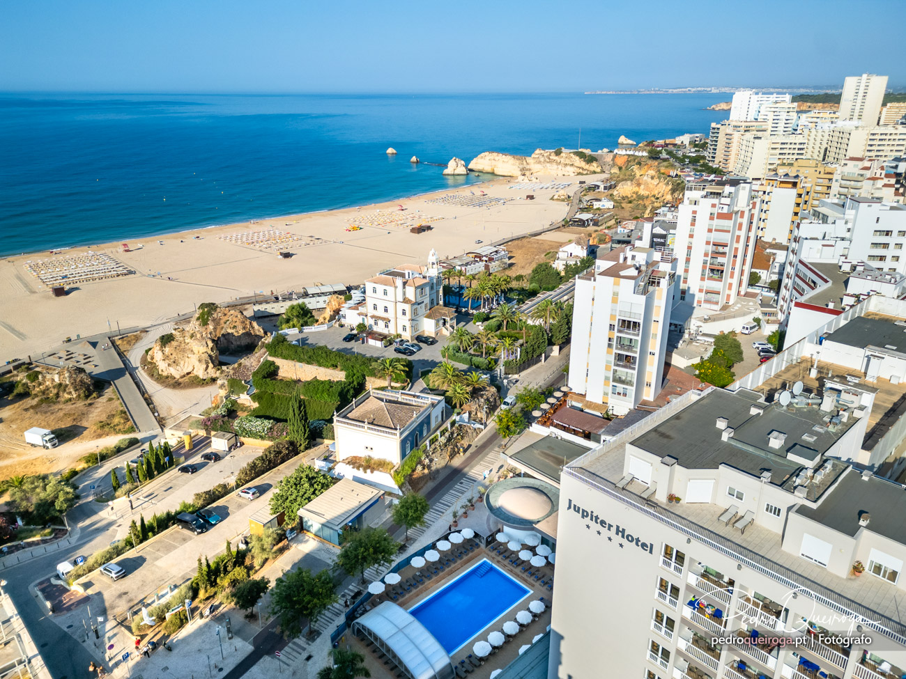 Vista aérea do Jupiter Hotel com piscina, junto à praia de Praia da Rocha e formações rochosas douradas ao fundo