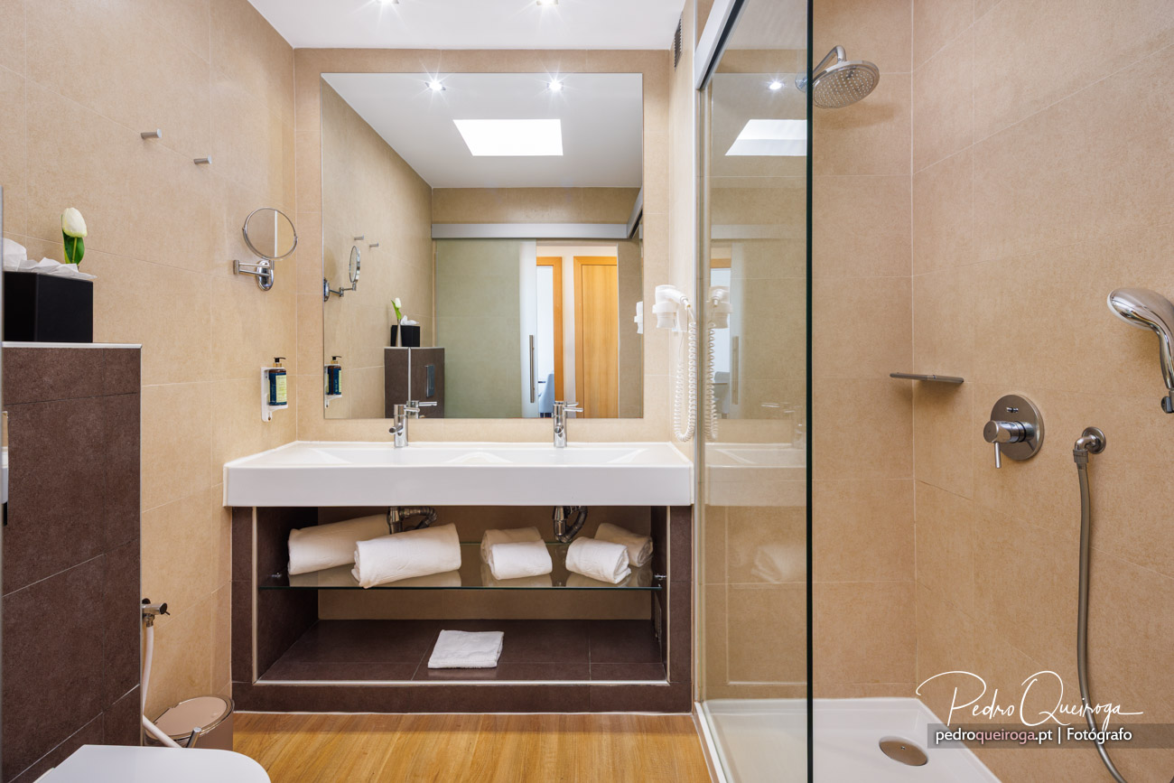 Casa de banho moderna com tons bege, lavatório duplo, espelho amplo, duche com vidro e toalhas arrumadas.