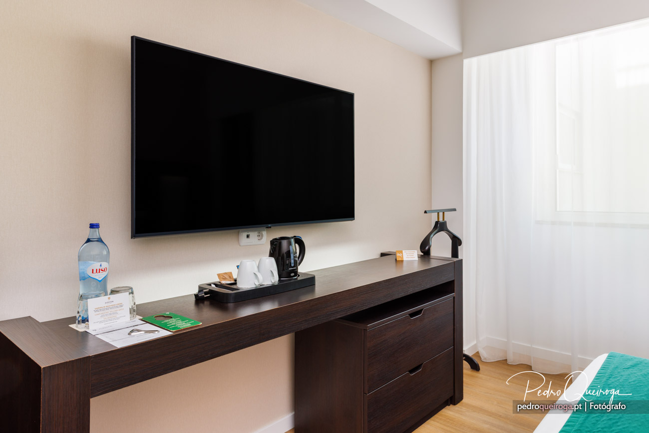 Quarto de hotel moderno com televisão de ecrã plano na parede, móvel escuro com chaleira e garrafa de água