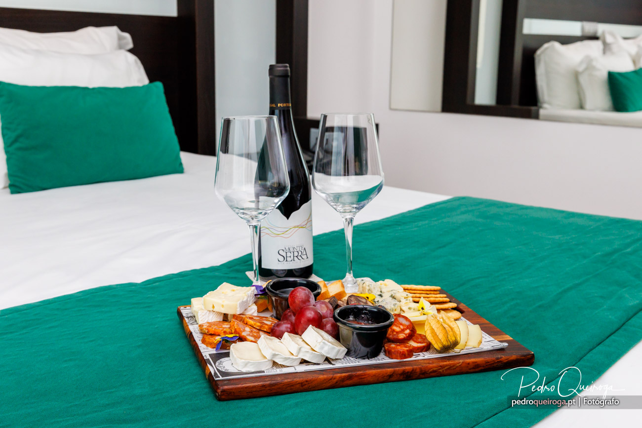 Tábua de queijos e fruta com vinho sobre cama verde em quarto elegante, fotografia de Pedro Queiroga