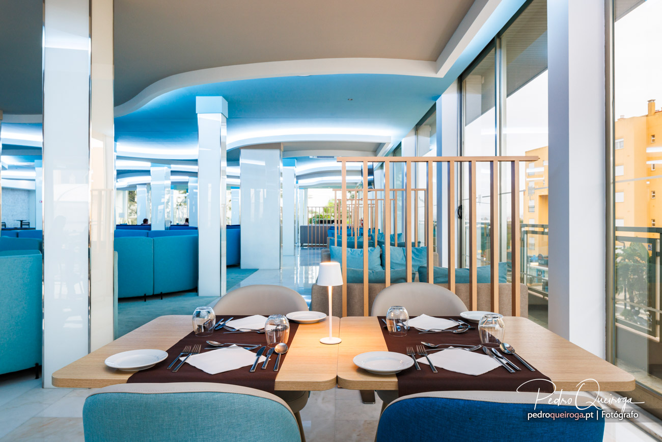 Mesa de restaurante moderna com cadeiras azuis e divisória em madeira, teto ondulado em tons azuis e brancos