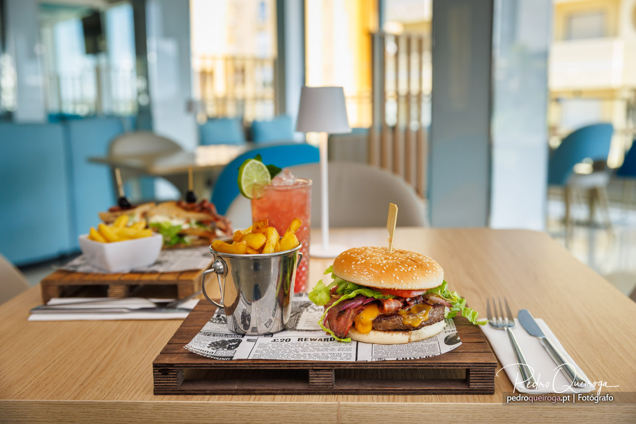 Hambúrguer suculento com bacon, batatas fritas e cocktail tropical servidos num restaurante moderno e luminoso