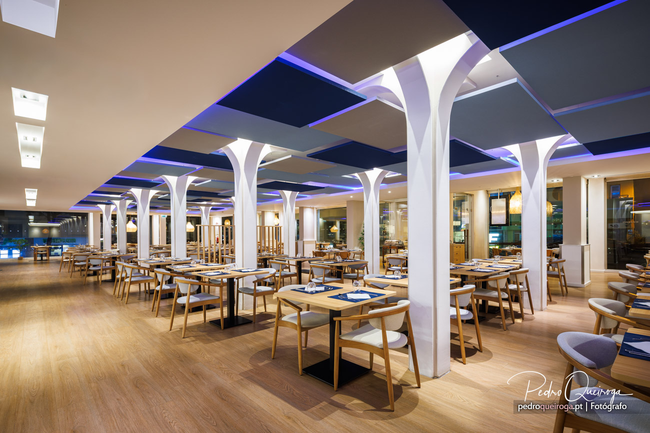 Restaurante moderno com colunas brancas elegantes e iluminação LED azul, ideal para hotéis contemporâneos