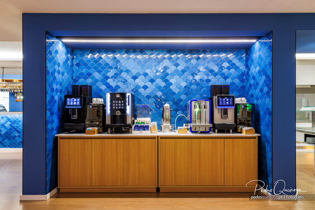 Balcão de café moderno com máquinas profissionais sobre móvel em madeira e parede azul com padrão de escamas decorativas