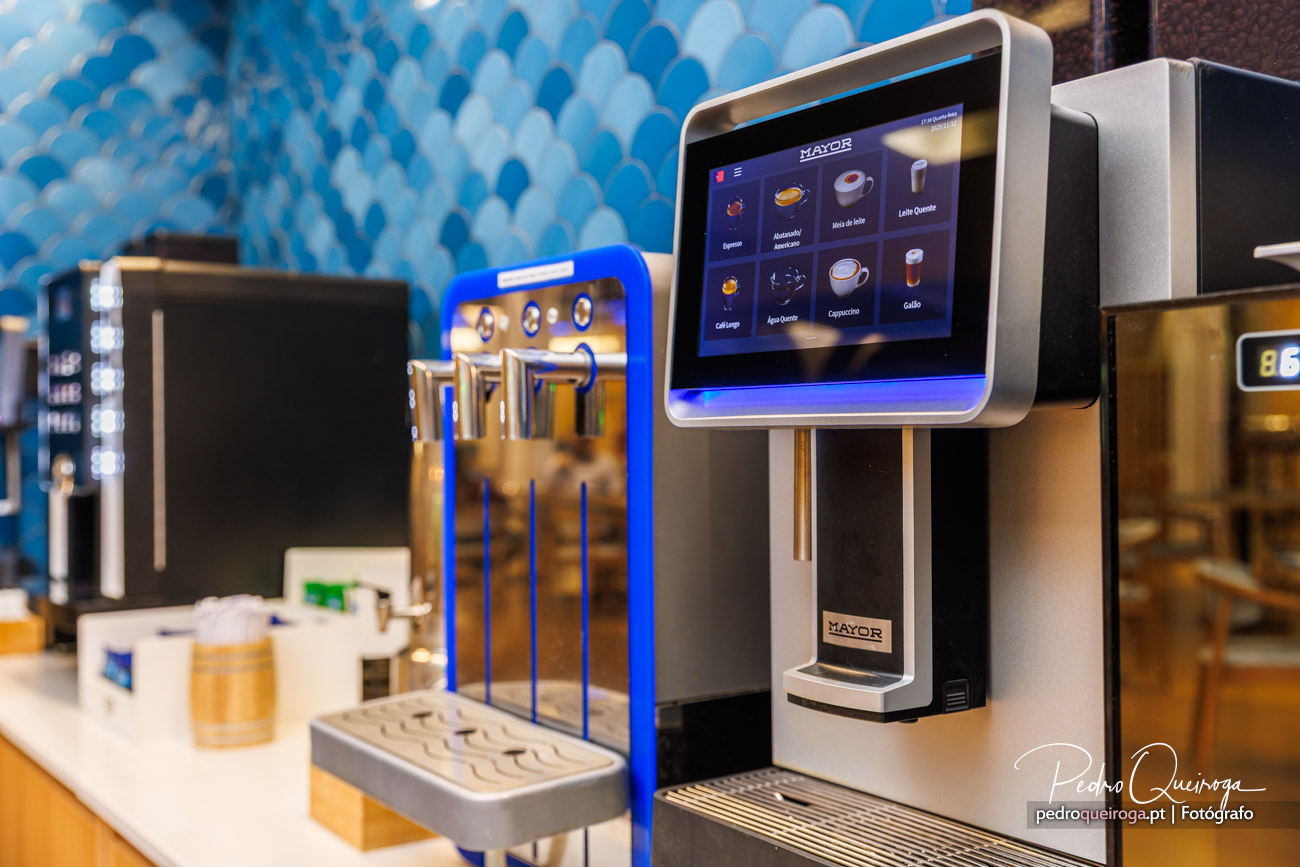 Máquina de café automática com ecrã tátil e parede decorativa azul em tons escamados ao fundo
