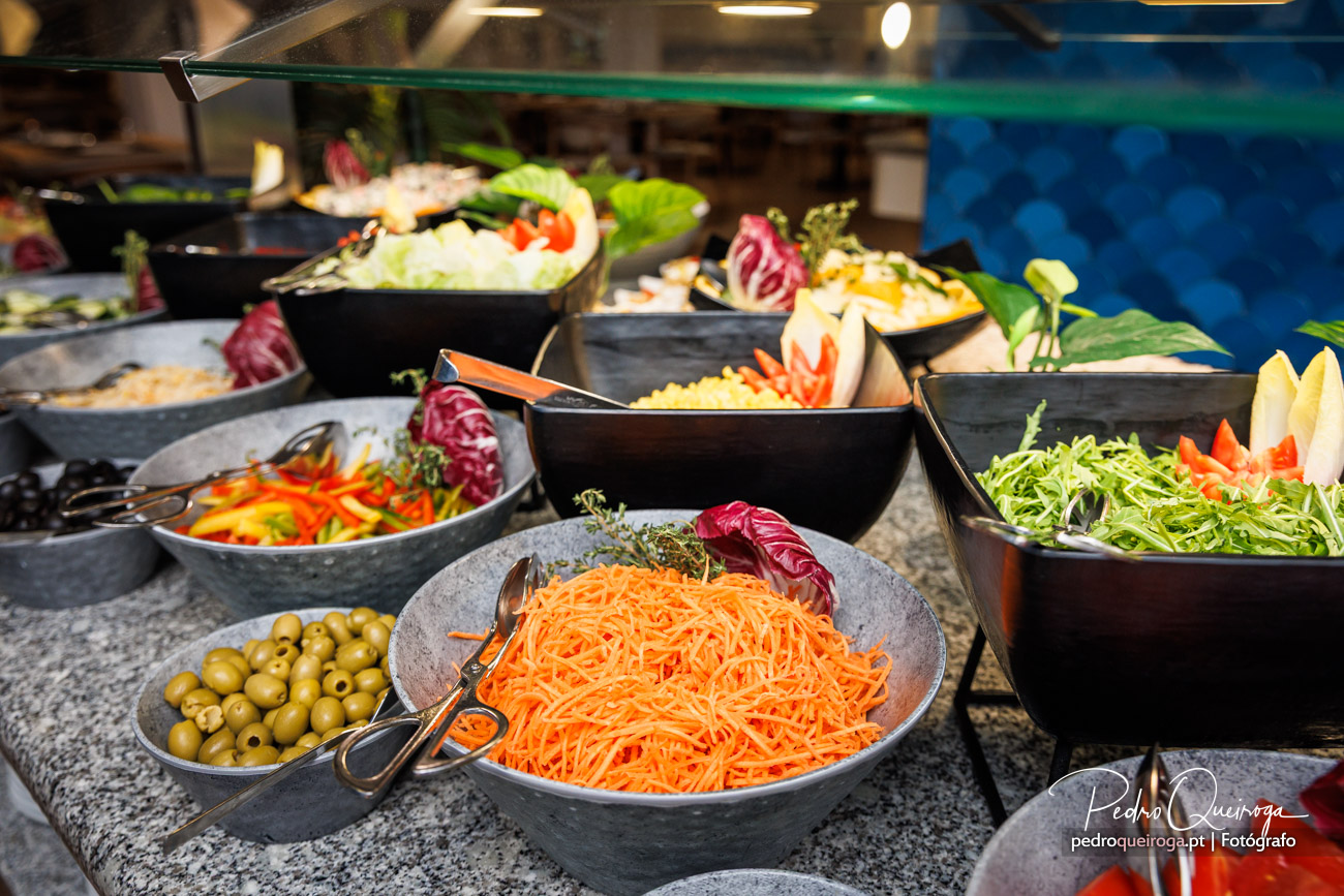 Buffet de saladas variadas em tigelas pretas com cenoura ralada, alfaces, azeitonas e vegetais frescos coloridos