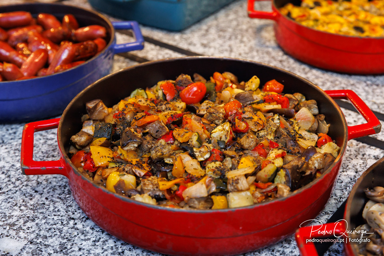 Tacho vermelho com salteado de legumes coloridos e carne sobre bancada de cozinha com outros pratos ao fundo