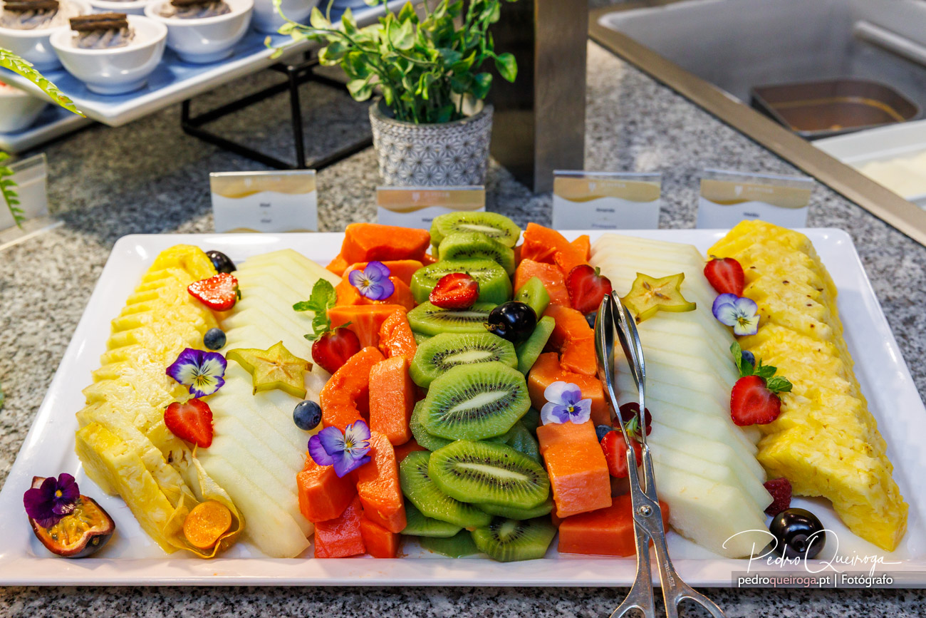 Travessa de fruta tropical cortada e disposta em arco-íris: ananás, melão, kiwi, mamão e morangos com flores comestíveis