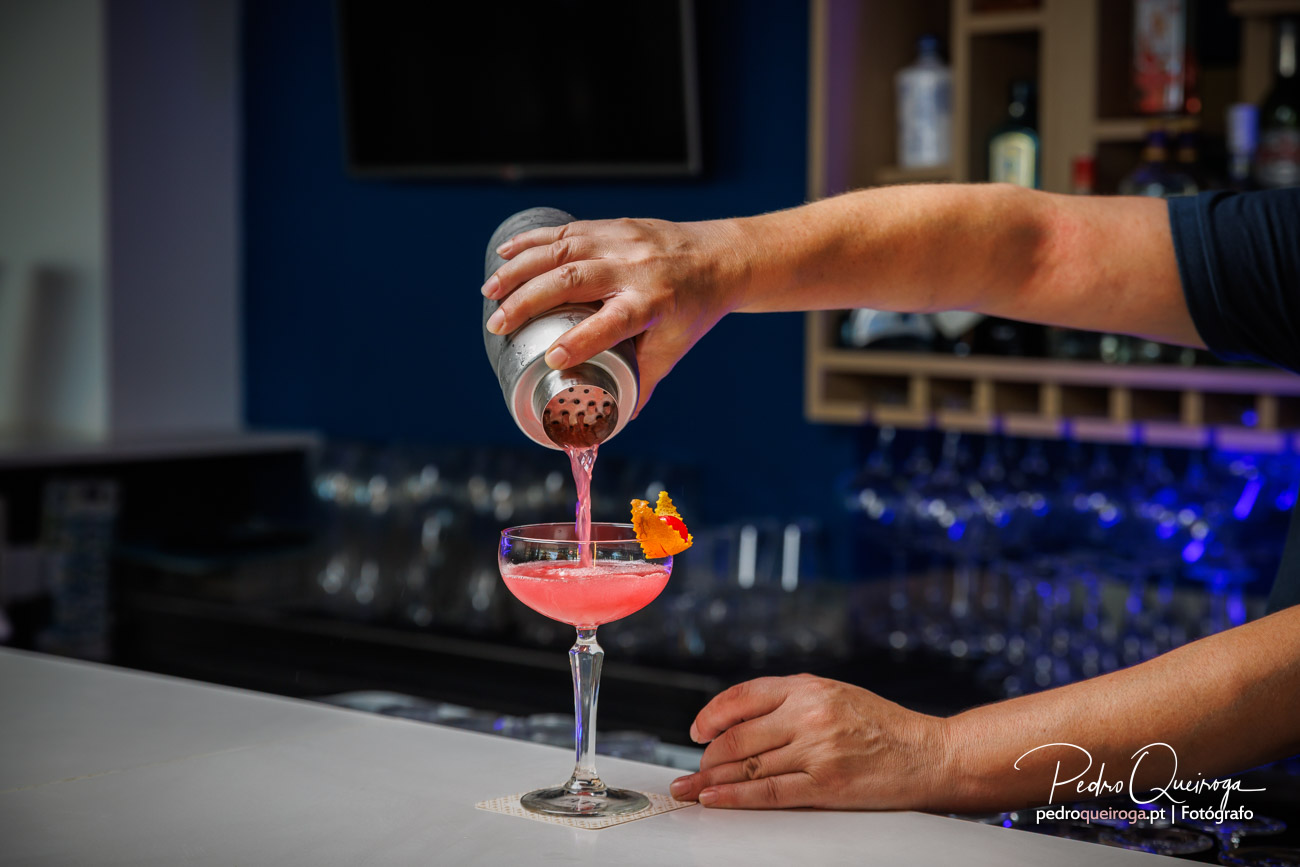 Barman a servir cocktail rosa num copo elegante, fotografia profissional de bar com iluminação ambiente azul