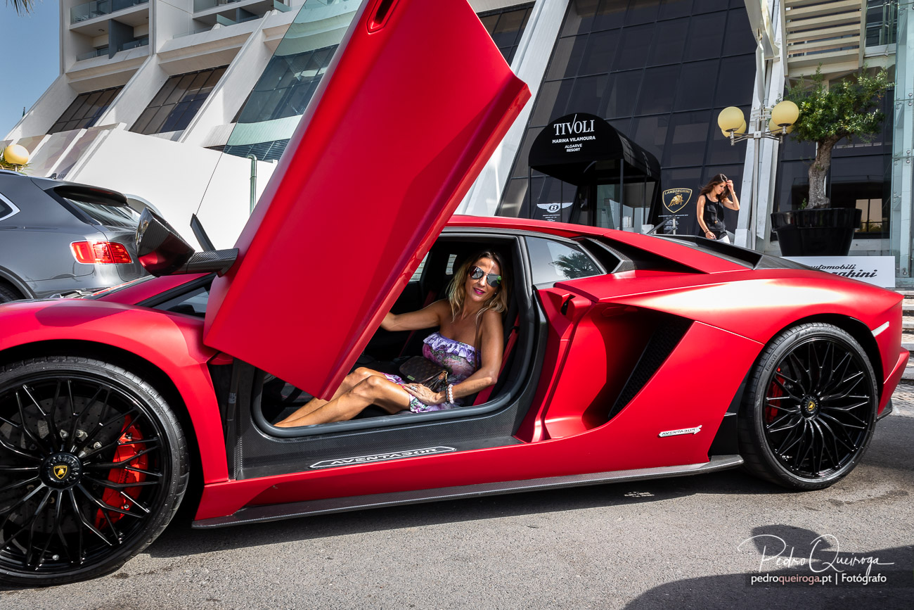 Lamborghini Aventador vermelho com portas abertas e mulher ao volante em frente a concessionária de luxo