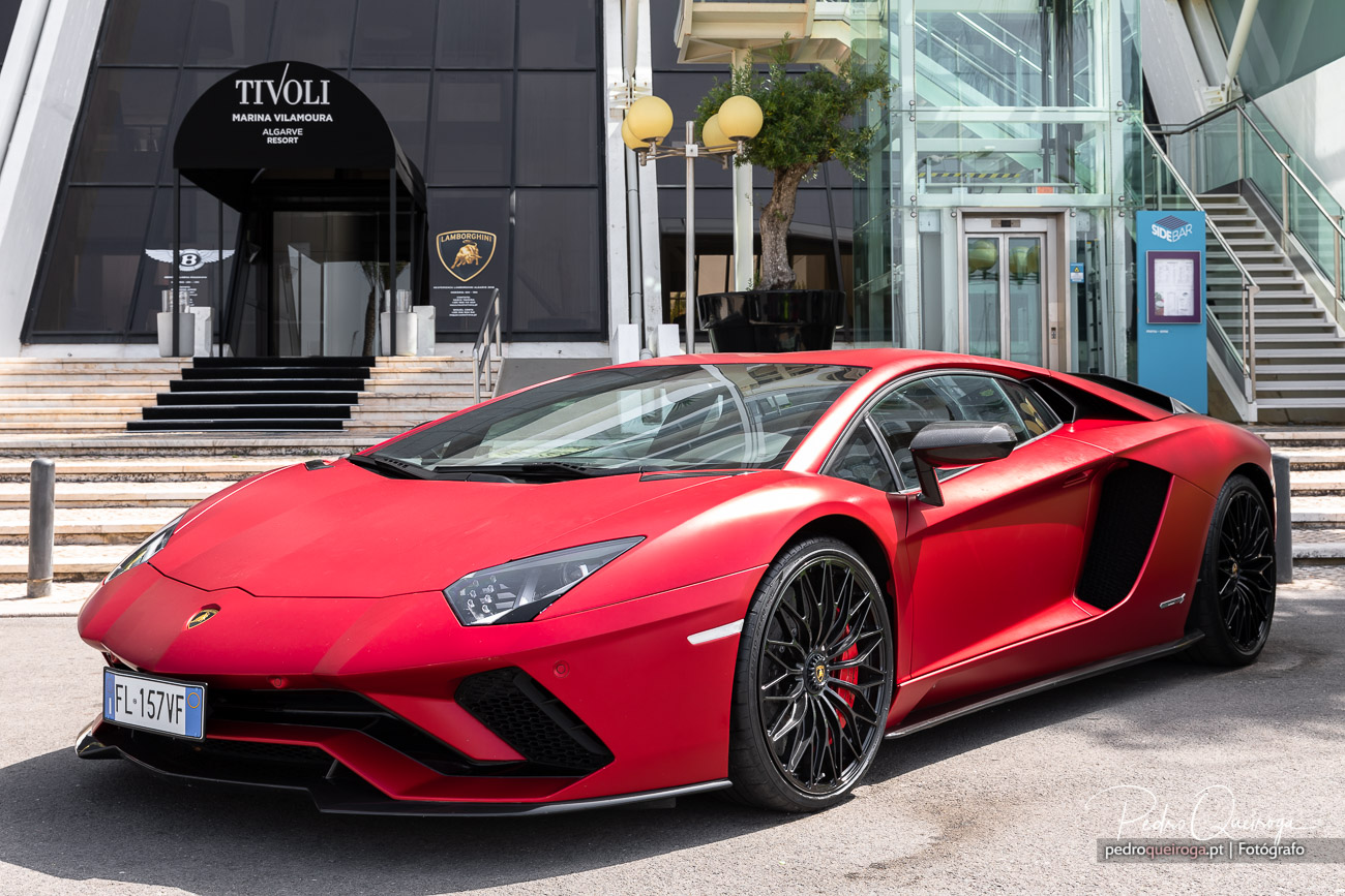 Lamborghini Aventador vermelho estacionado em frente à marina Tivoli com fachada moderna em vidro e escadas.