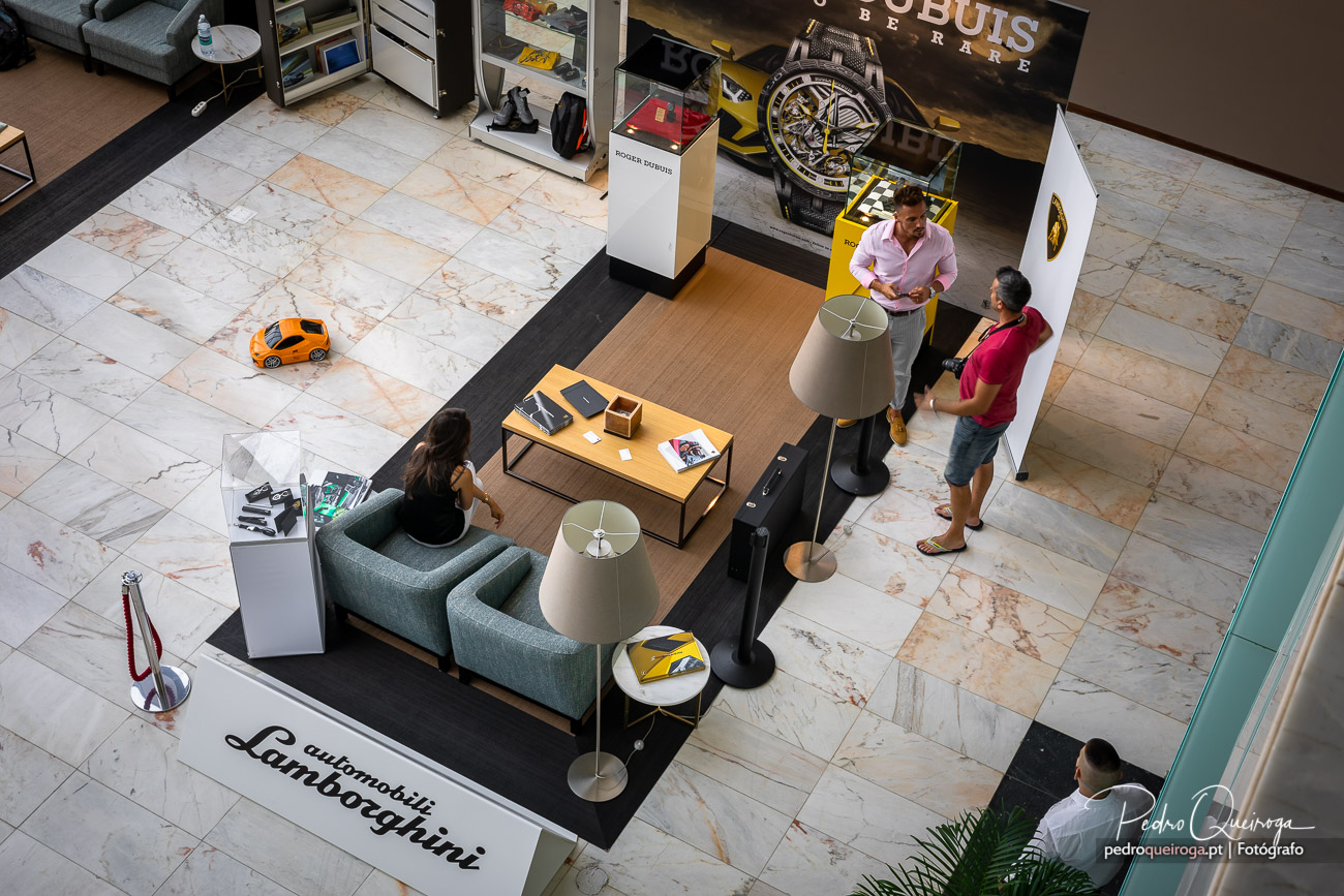 Vista aérea de stand Lamborghini num centro comercial, com clientes a conversar junto a uma área lounge moderna e elegante.