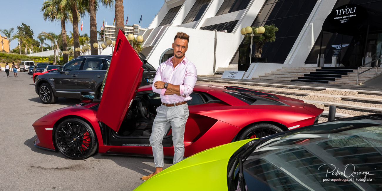 Fotografia de homem junto a superdesportivo vermelho com portas abertas em frente à Marina de Vilamoura