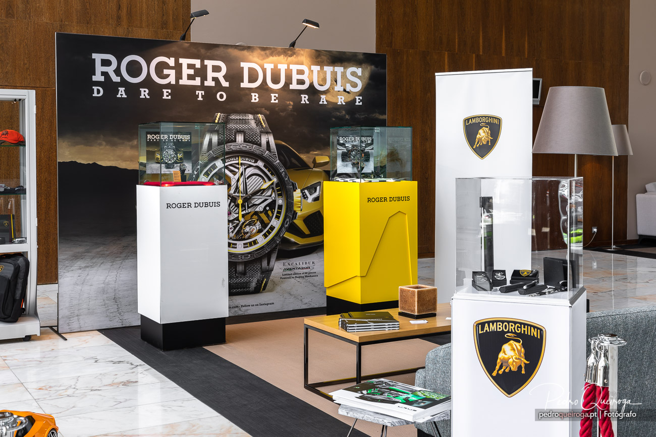 Espaço comercial elegante com expositor Roger Dubuis iluminado e vitrines Lamborghini em ambiente moderno revestido a madeira