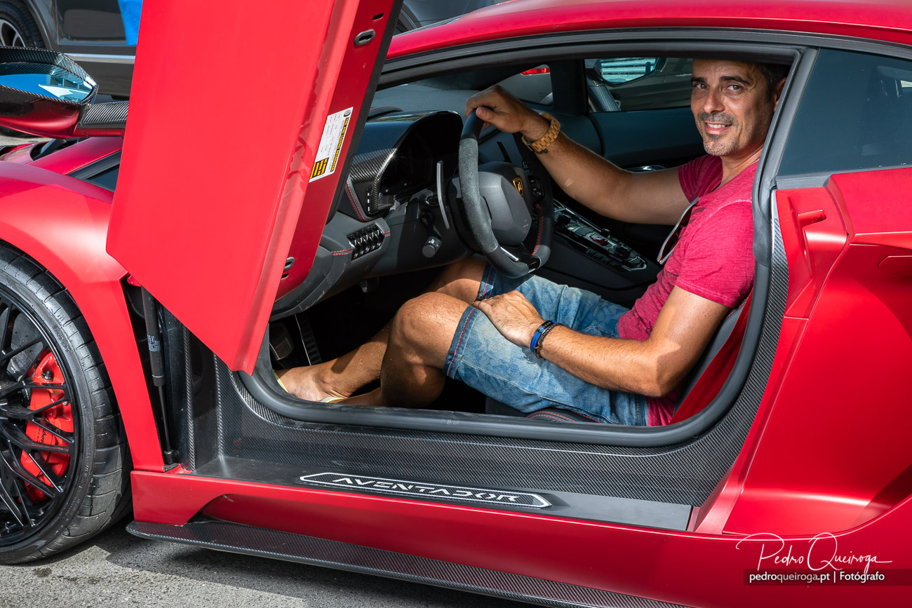 Homem sorridente ao volante de um Lamborghini Aventador vermelho com porta aberta e detalhes em fibra de carbono