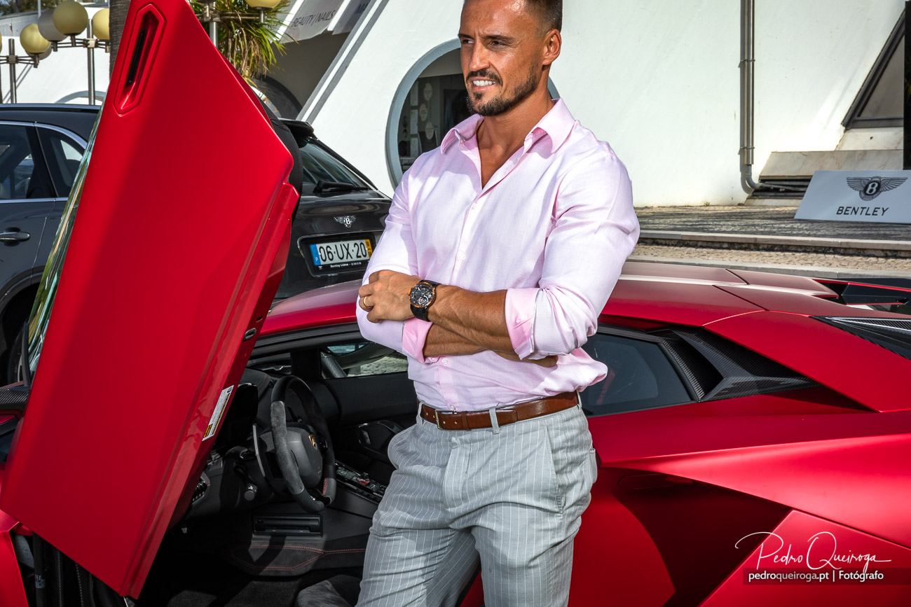Homem elegante junto a superdesportivo vermelho com portas abertas em evento de luxo no Algarve