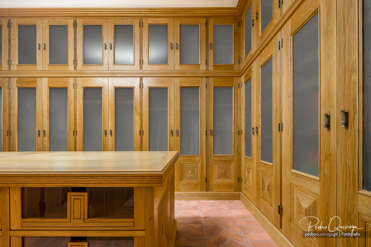 Closet luxuoso em madeira de carvalho com portas de vidro fosco, detalhes geométricos e pavimento em terracota rosa.