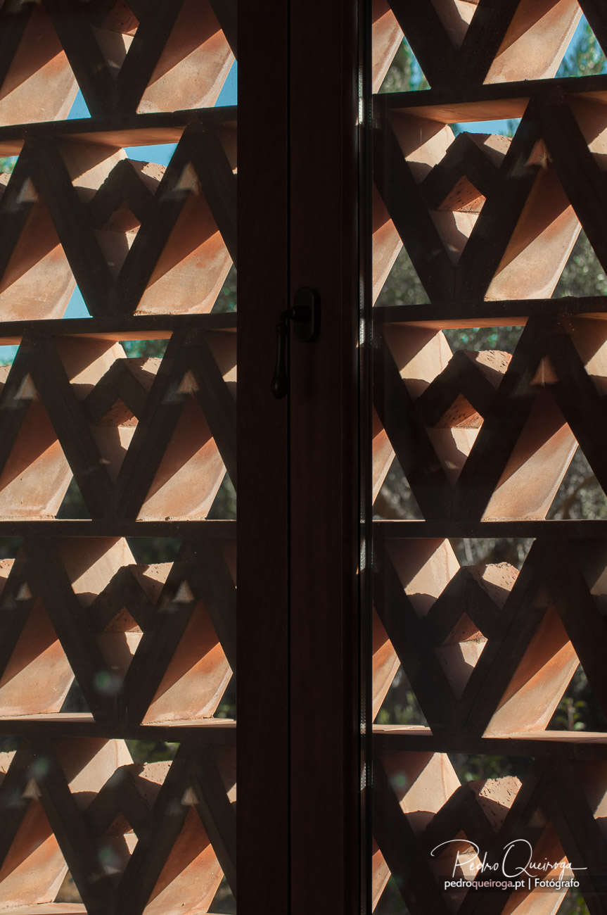 Porta com padrão geométrico em madeira escura, formando estrelas vazadas que filtram a luz natural do exterior
