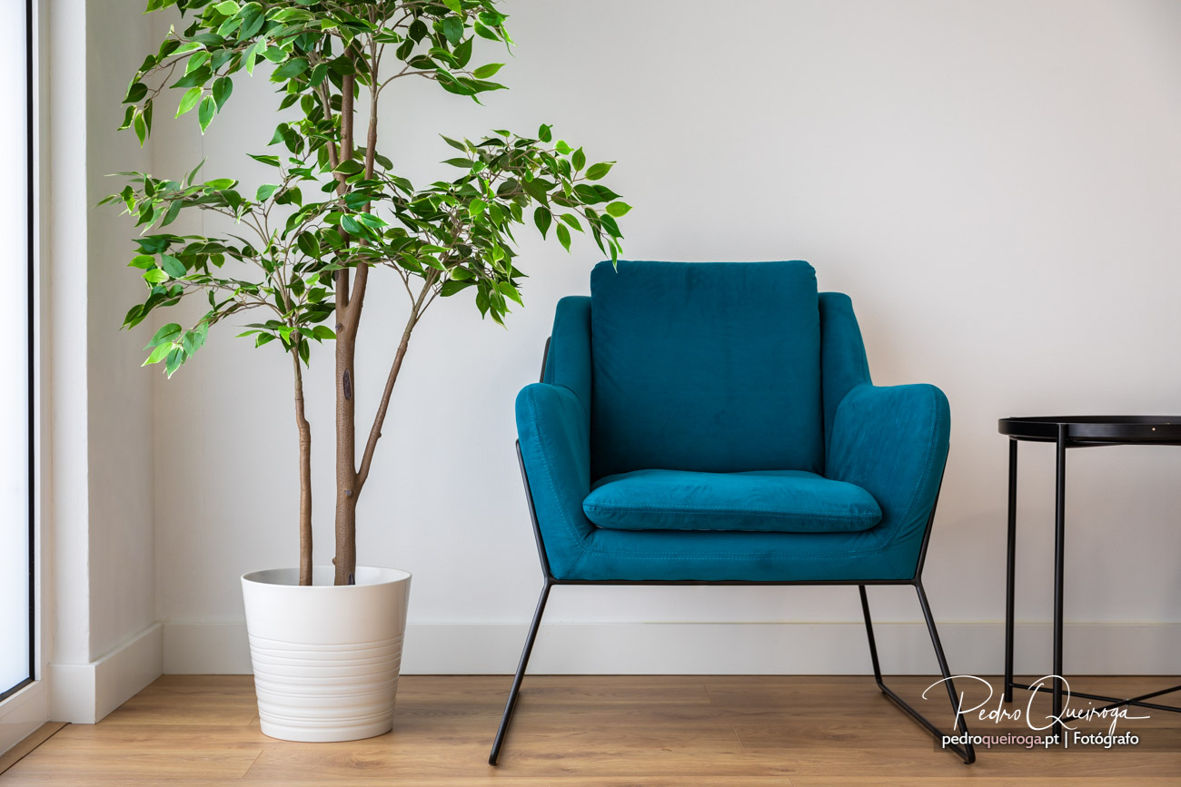Poltrona azul-petróleo moderna junto a planta verde em vaso branco sobre pavimento de madeira clara