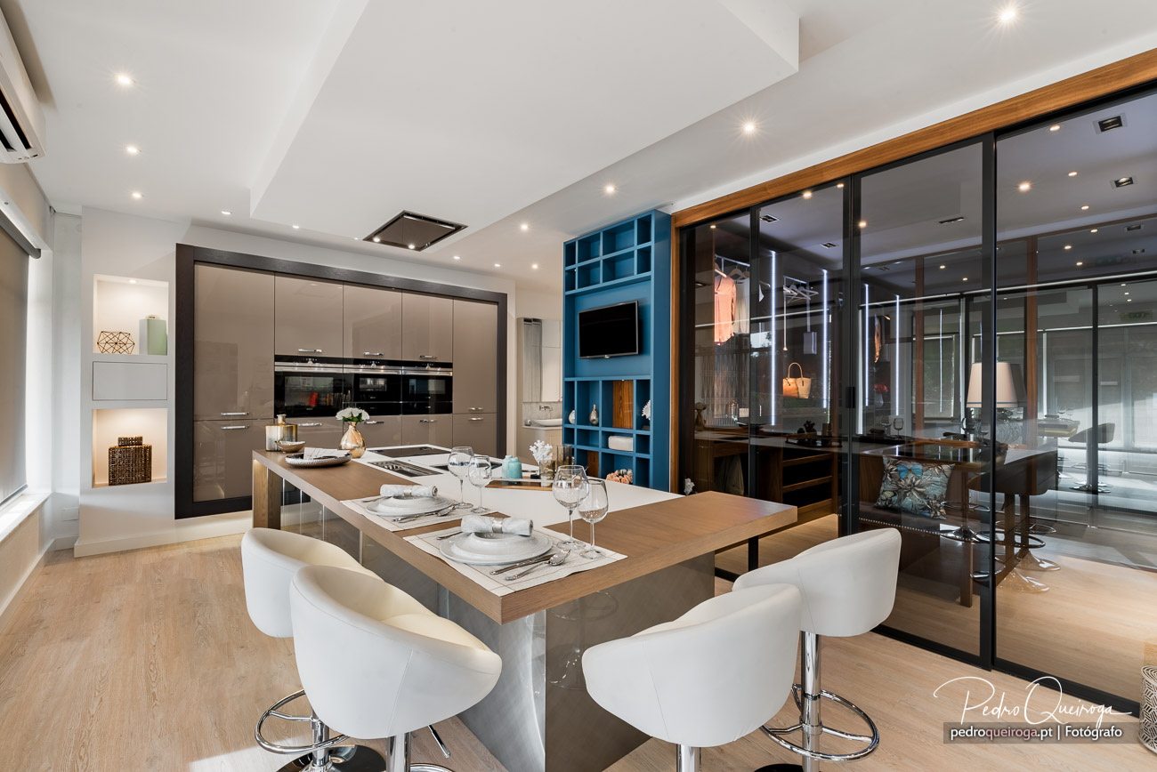 Cozinha moderna com ilha central, cadeiras brancas, estante azul e divisória de vidro para sala de jantar elegante