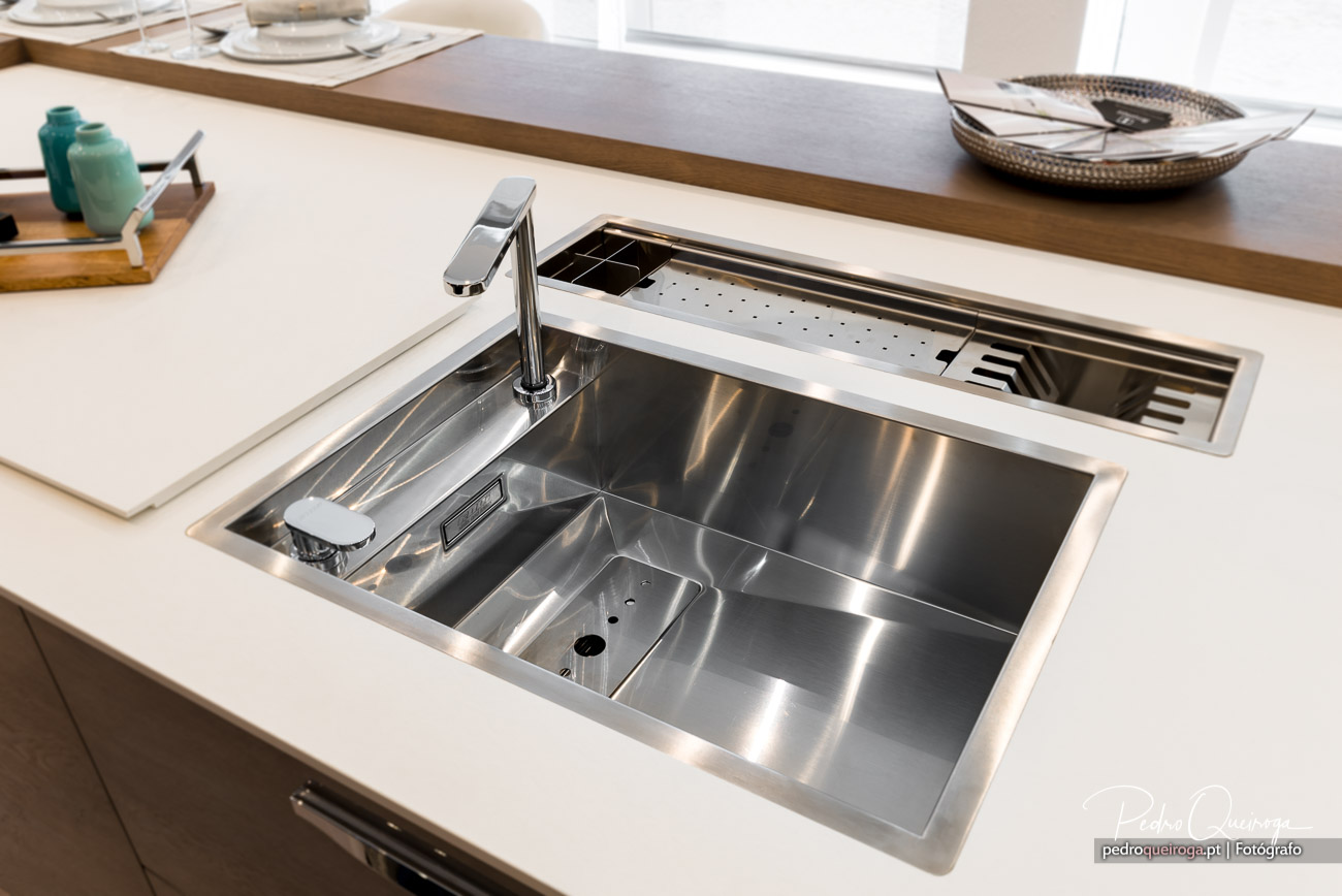 Lava-louça moderna em inox embutida em bancada branca, com torneira cromada e acessórios práticos na decoração de cozinha.
