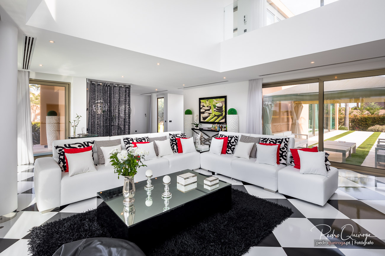 Sala de estar moderna com sofás brancos, almofadas vermelhas e pretas, mesa de centro preta e amplas portas envidraçadas.