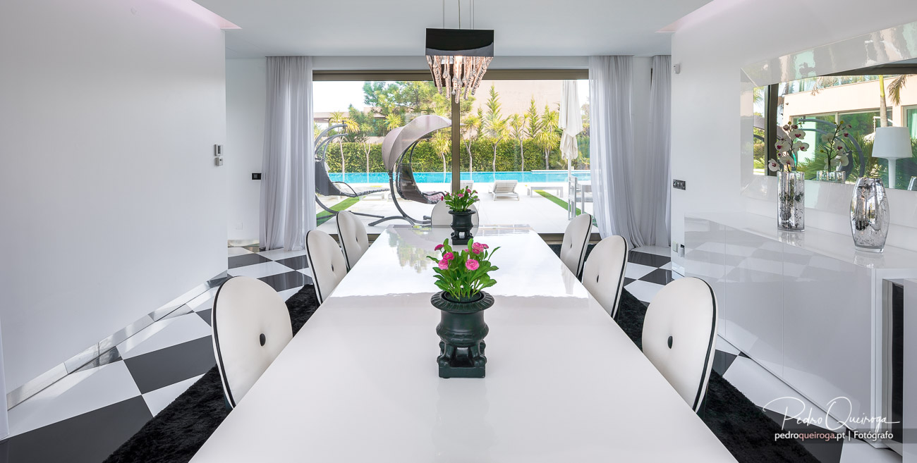 Sala de jantar moderna com mesa branca, cadeiras elegantes e vista para piscina em composição fotográfica de luxo.