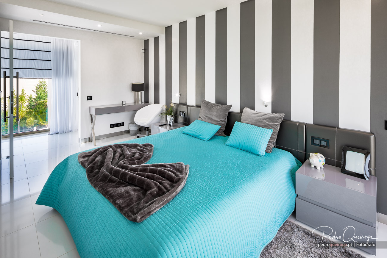 Quarto moderno com decoração minimalista, cama turquesa e parede com faixas verticais cinzentas e brancas