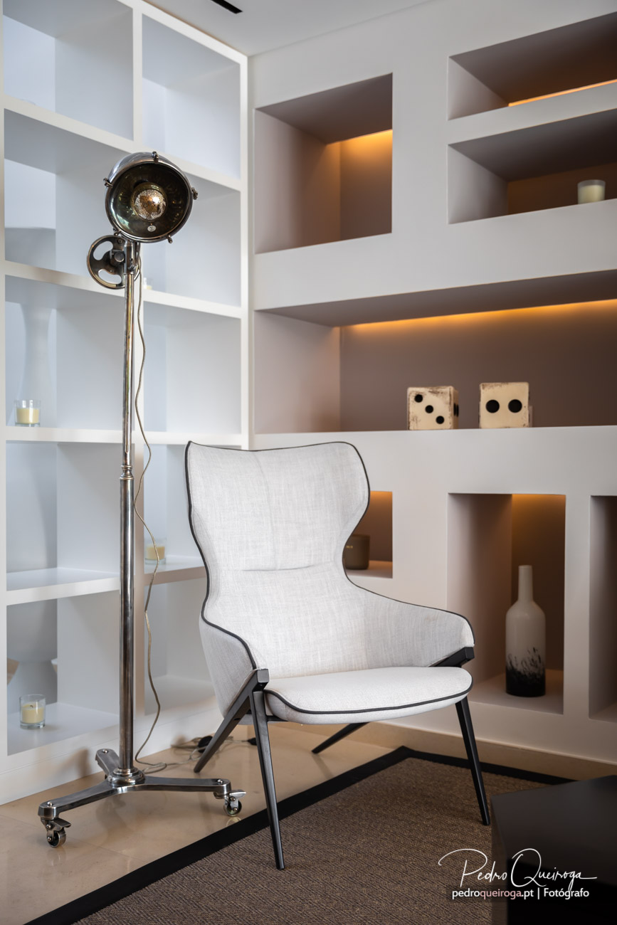 Cadeira branca moderna junto a estante com nichos iluminados e candeeiro industrial cromado em sala contemporânea