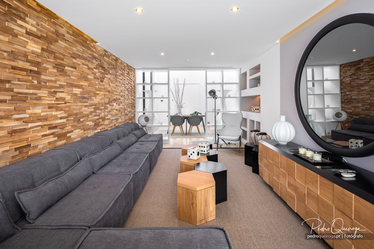 Sala de estar moderna com parede em madeira, sofá cinzento e espelho circular, destacando o imóvel contemporâneo