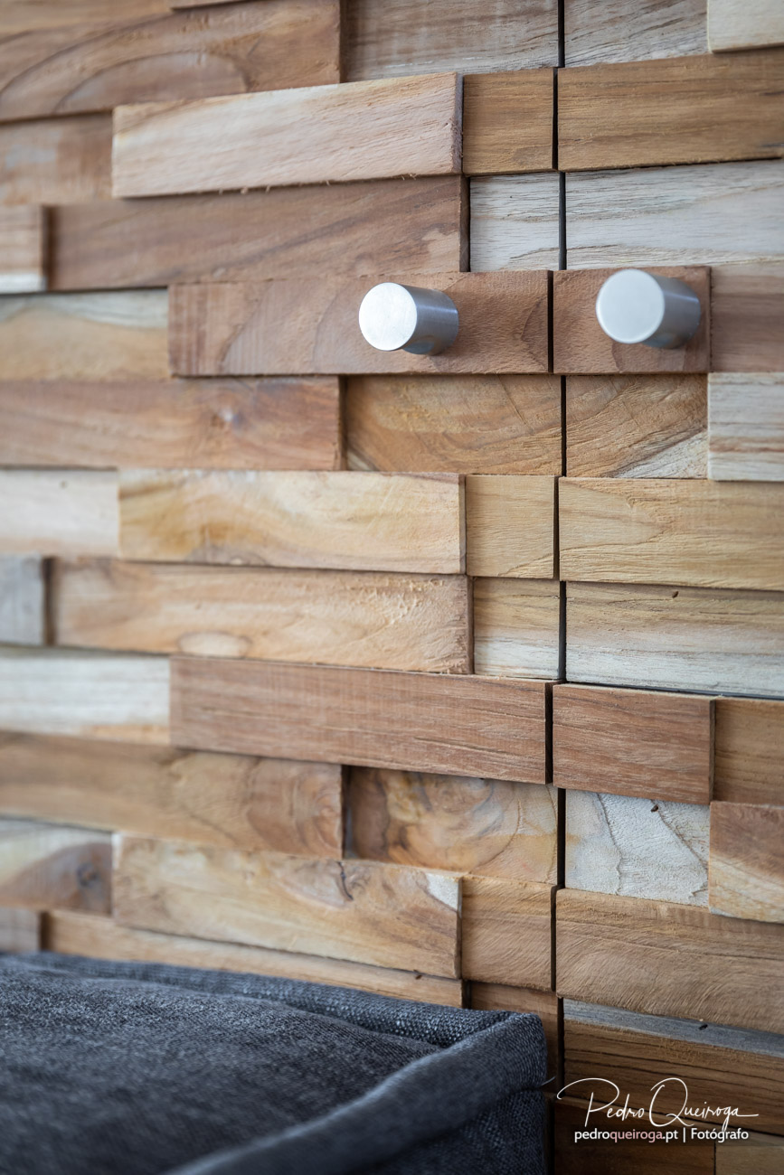 Parede revestida com ripas de madeira em tons naturais e dois puxadores redondos metálicos prateados ao centro