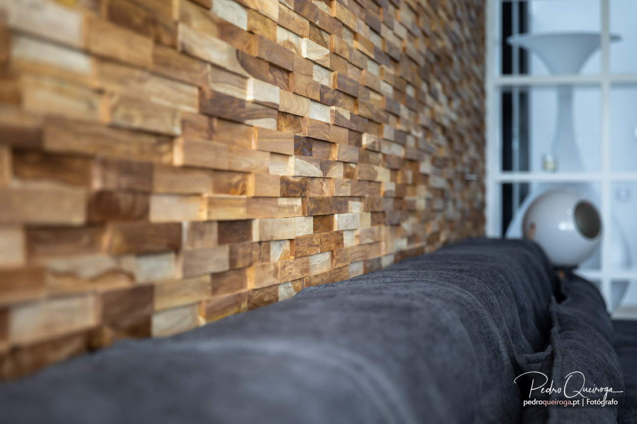 Parede de madeira tridimensional em tons naturais com sofá cinzento e estante branca ao fundo num interior moderno