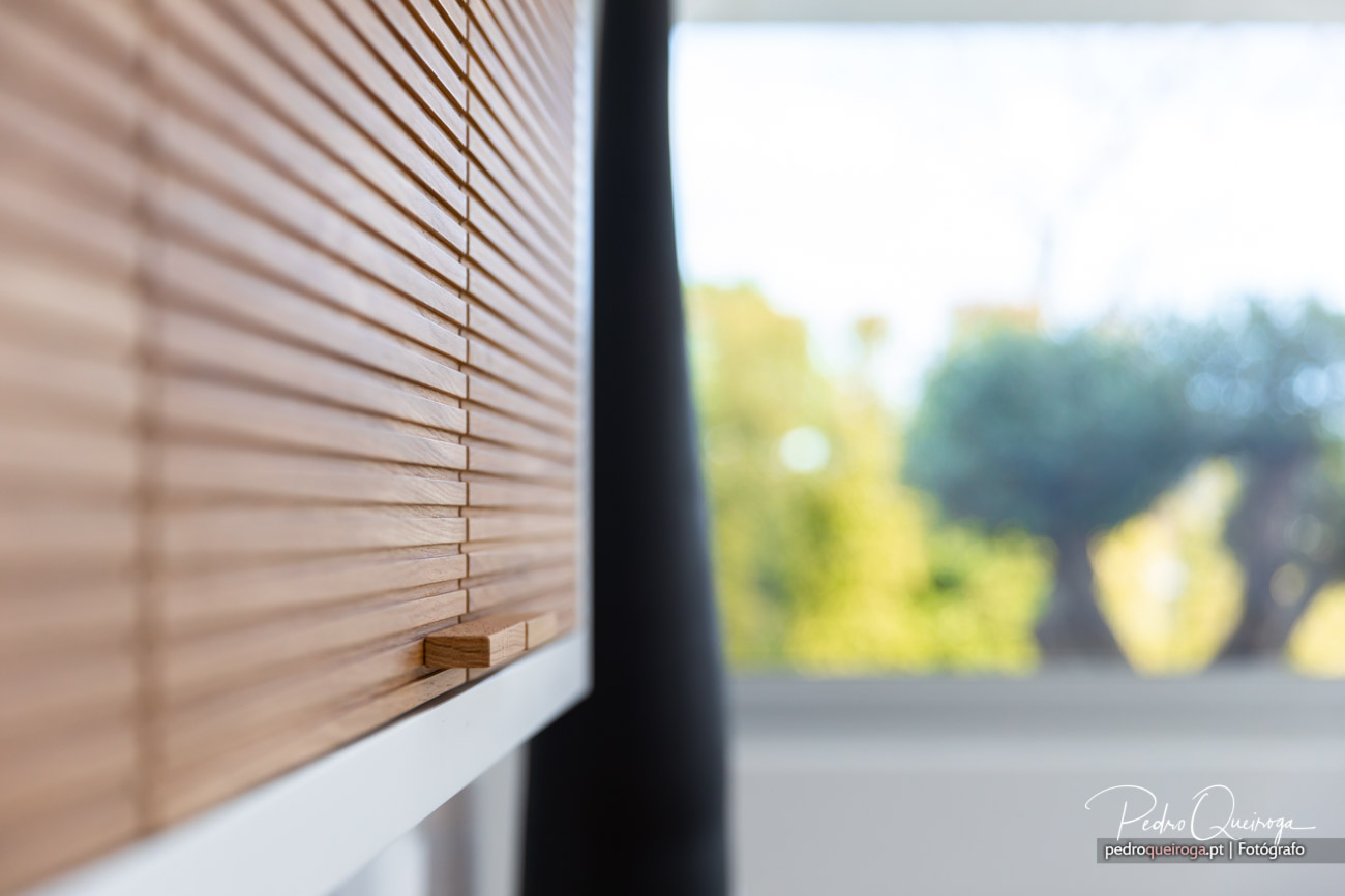 Estores de madeira numa janela moderna com vista desfocada para vegetação exterior e luz natural suave