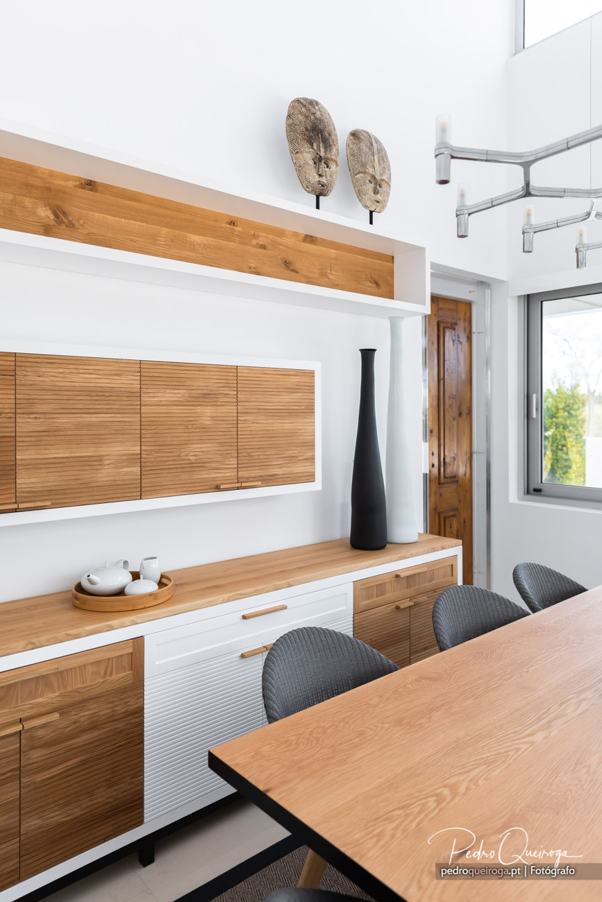 Sala de jantar moderna com mesa de madeira, cadeiras cinzentas e móvel com detalhes em madeira e branco.
