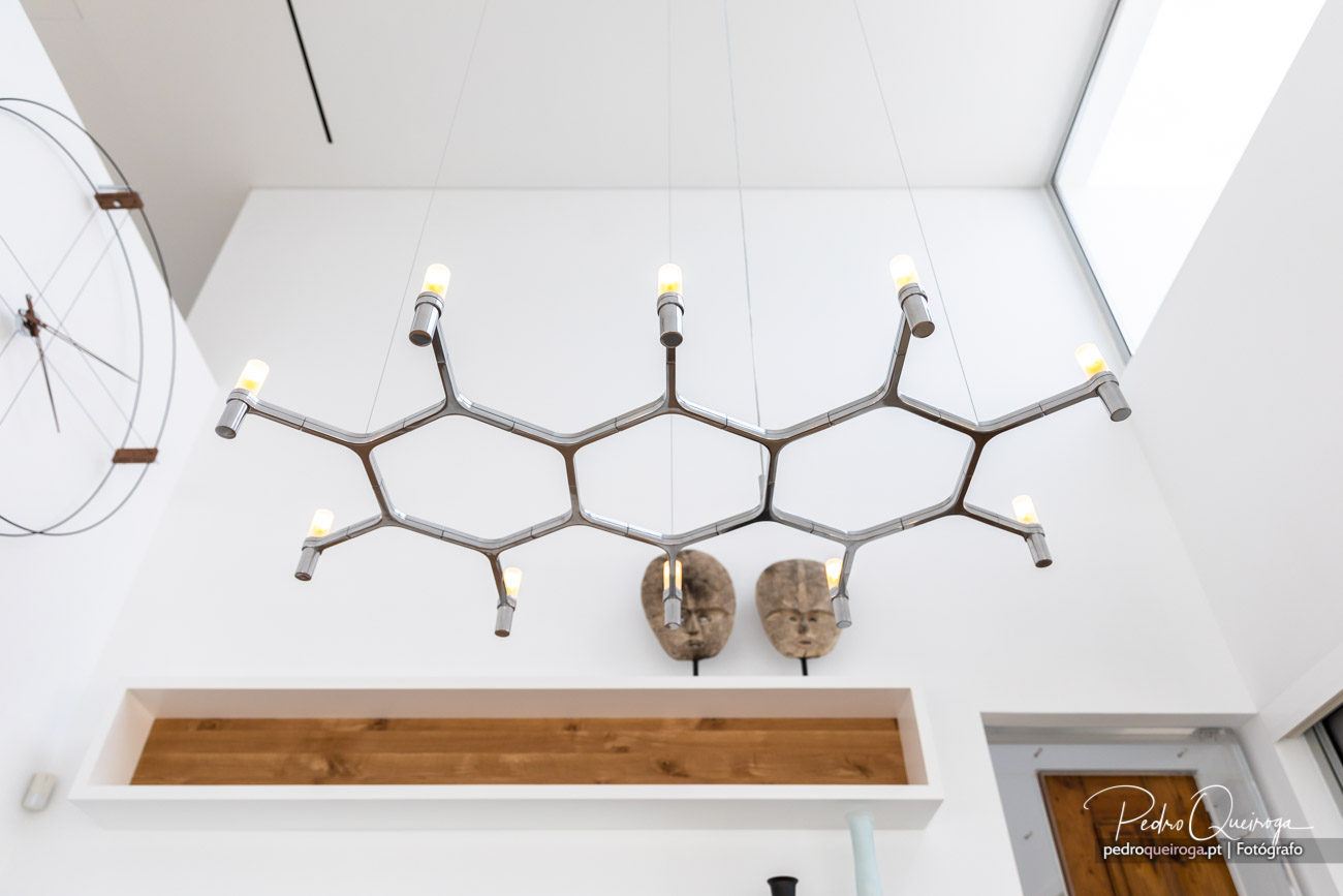 Candeeiro suspenso moderno em estrutura metálica geométrica hexagonal com lâmpadas expostas e máscaras decorativas na parede branca