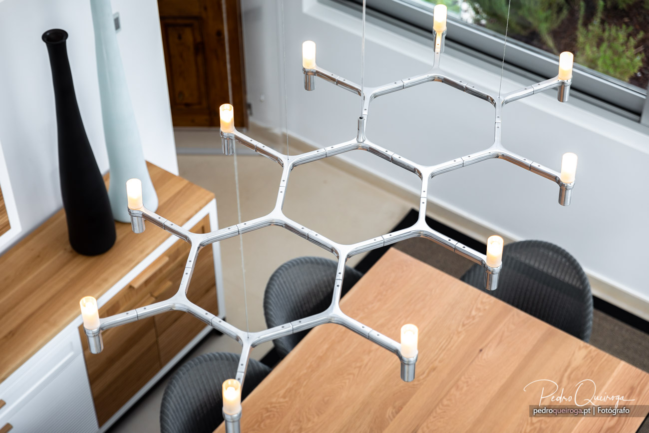 Divisória modular hexagonal em acrílico com velas suspensa sobre mesa de madeira em sala luminosa e moderna