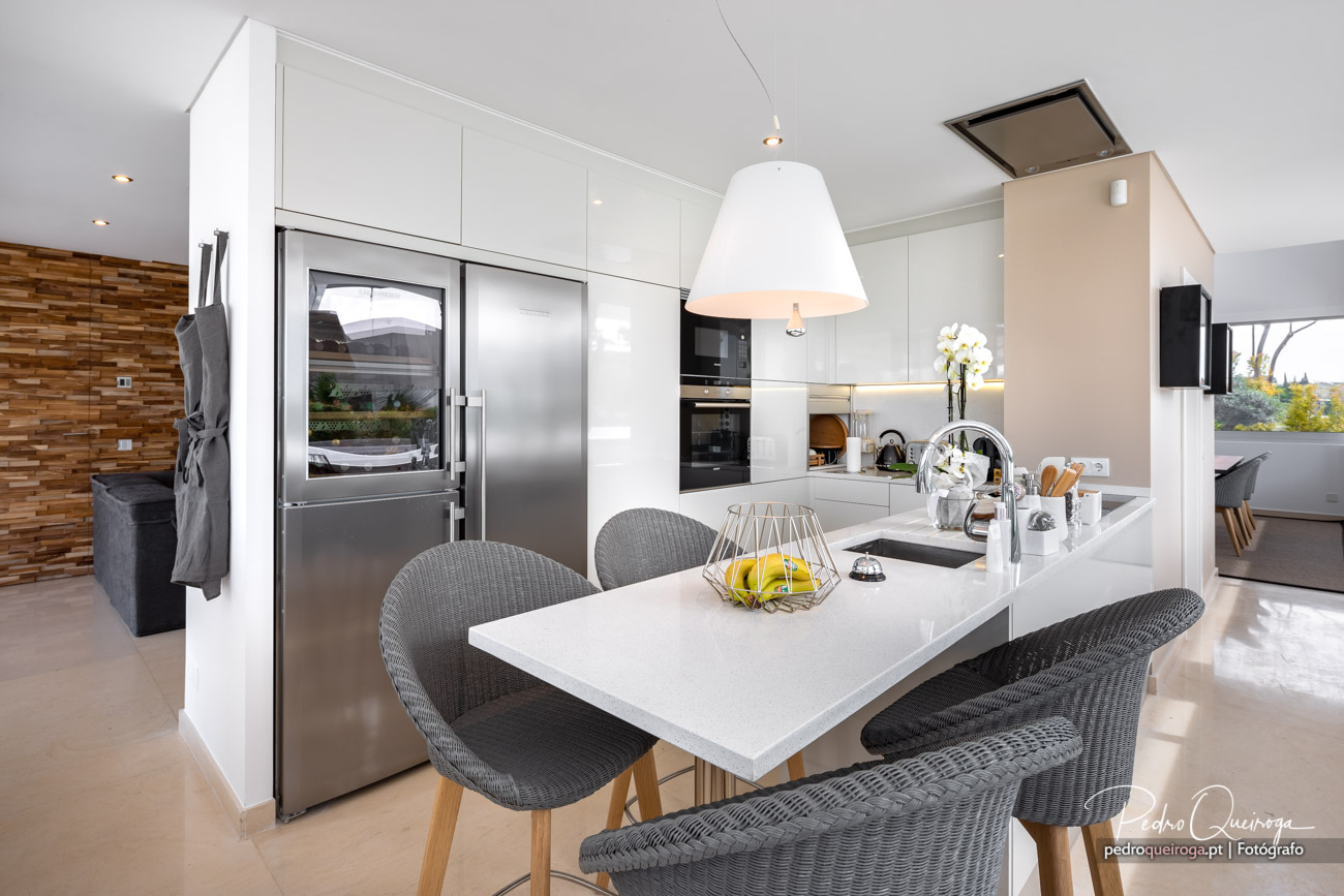 Cozinha moderna com ilha central, acabamentos brancos e detalhes em madeira, destacada em produções fotográficas de interiores.